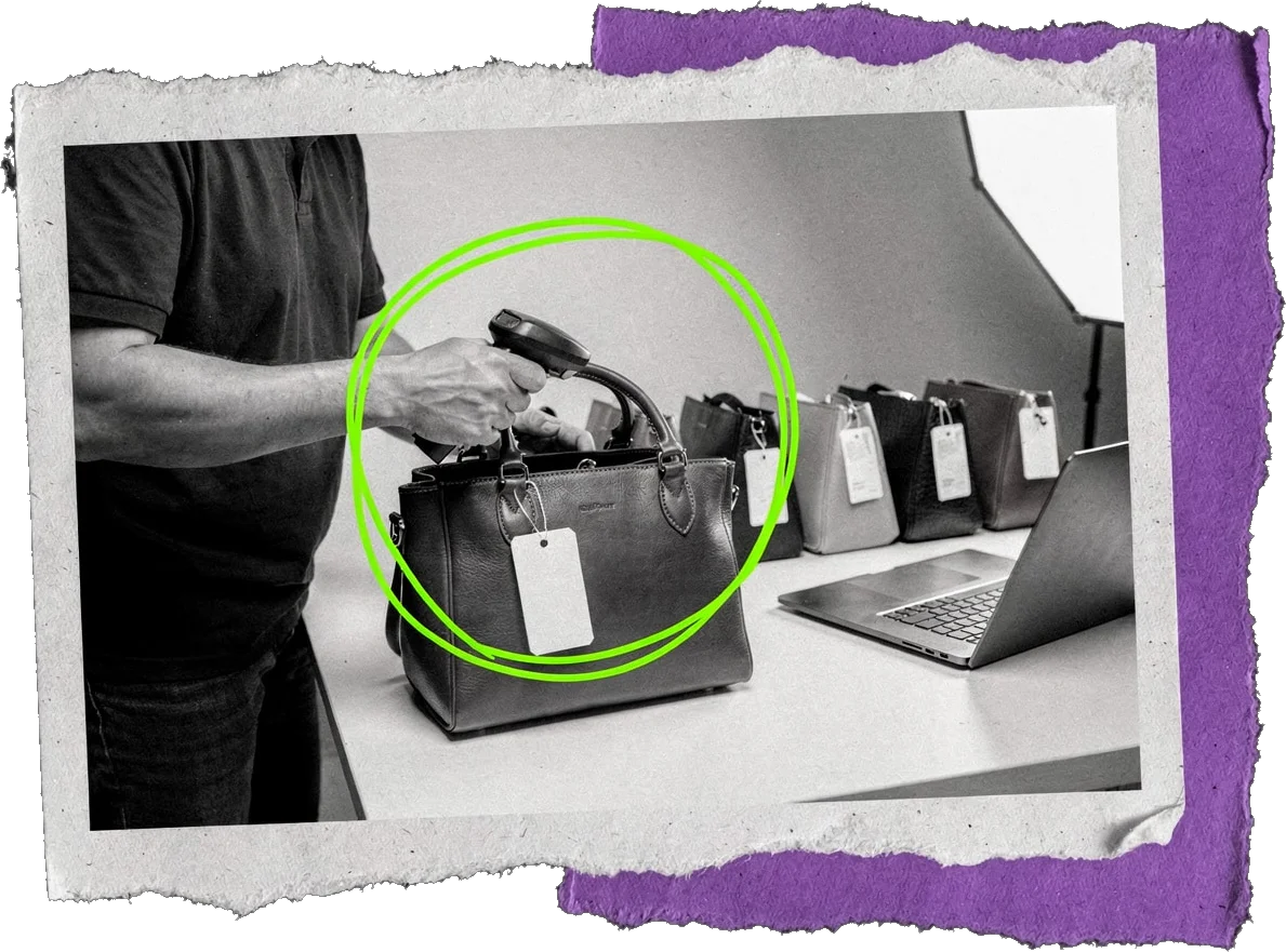 Black-and-white photo of a person scanning the tag on a handbag at a table with a laptop and more tagged bags in a row; the bag is circled in green.