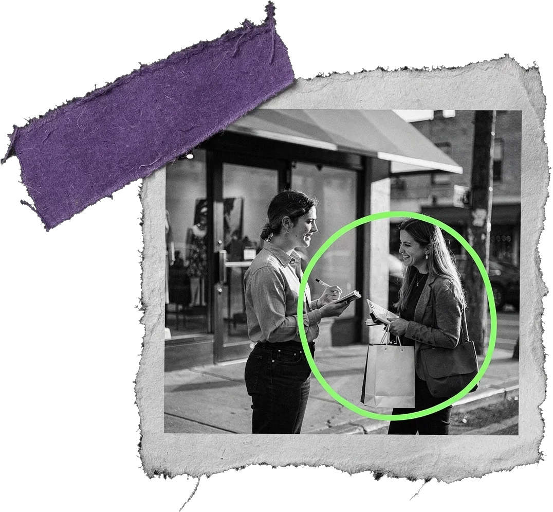 Black-and-white photo of two women talking on a shopping street; one holds a notebook and a paper bag, and the second woman is circled in green.