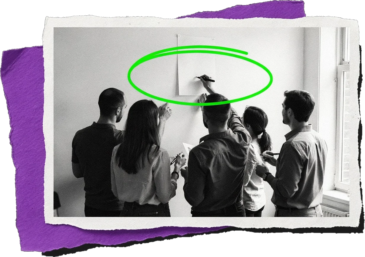 Black-and-white photo of six colleagues gathered at a wall, one writing on a sheet of paper that is circled in green.